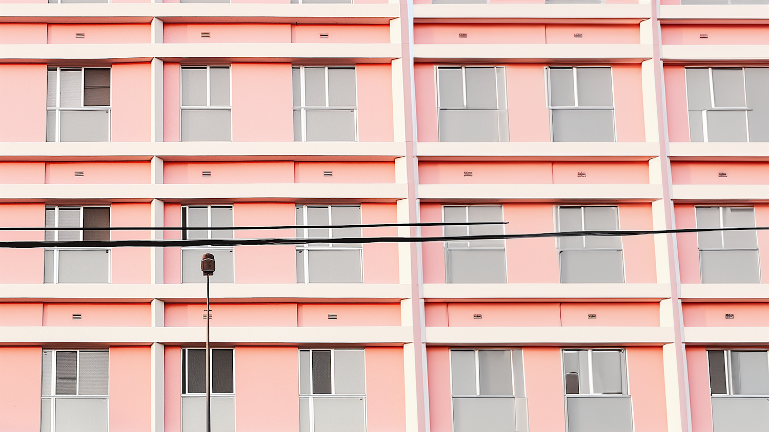 Fachada de prédio rosa com janelas e fios de energia passando à frente